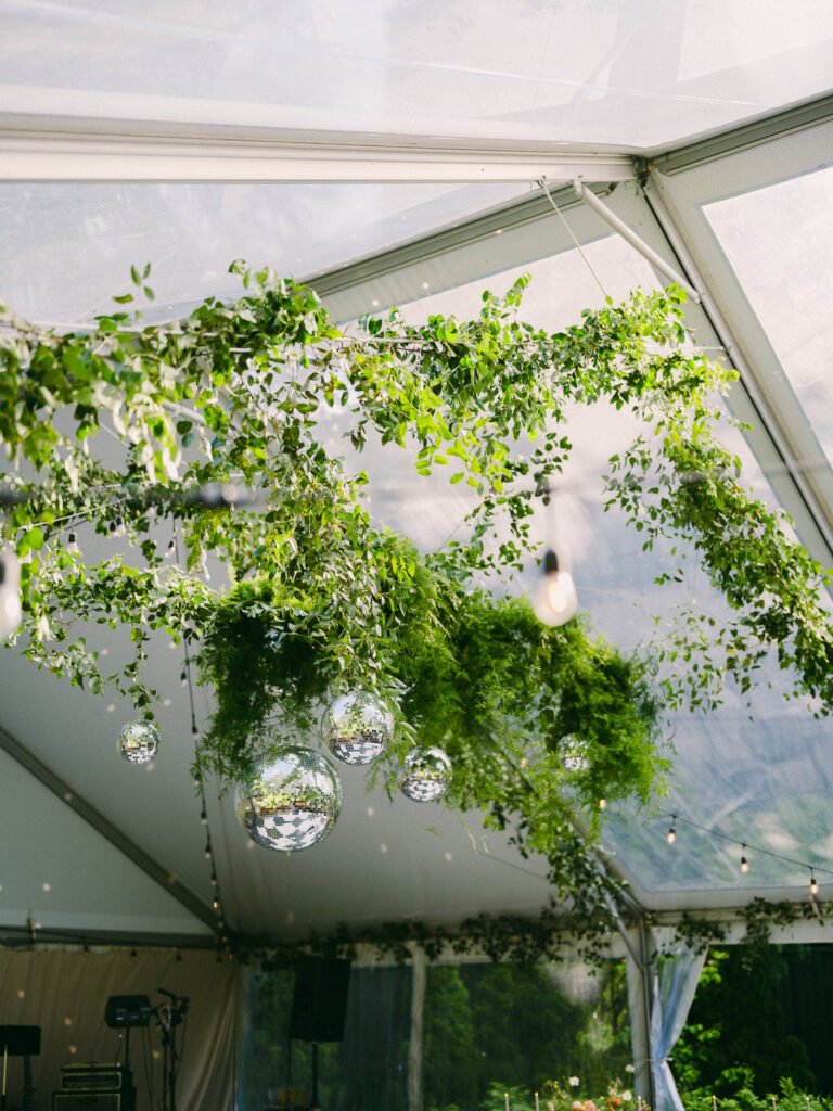 Greenery and disco balls hanging from the clear tent ceiling at a Griffin House wedding reception.