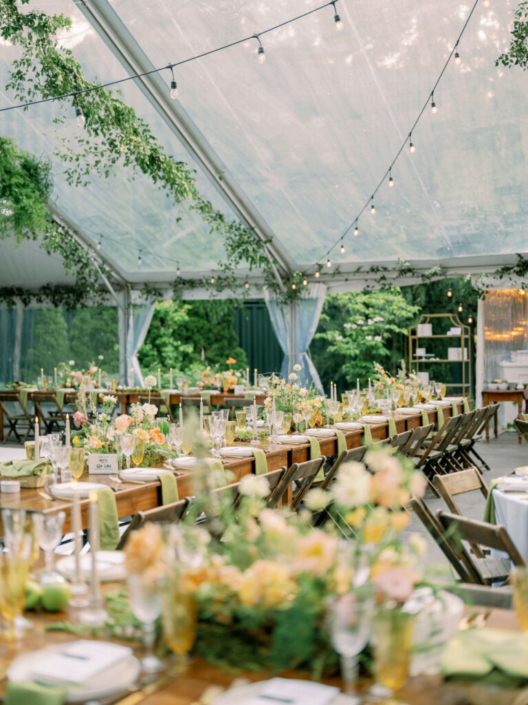 Long wooden tables arranged beneath a clear tent at the Griffin House, styled with florals, taper candles, and green linen runners.