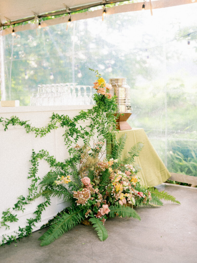 Floral installation at the bar during a Griffin House wedding reception, featuring cascading greenery and soft pastel blooms beneath a clear tent.
