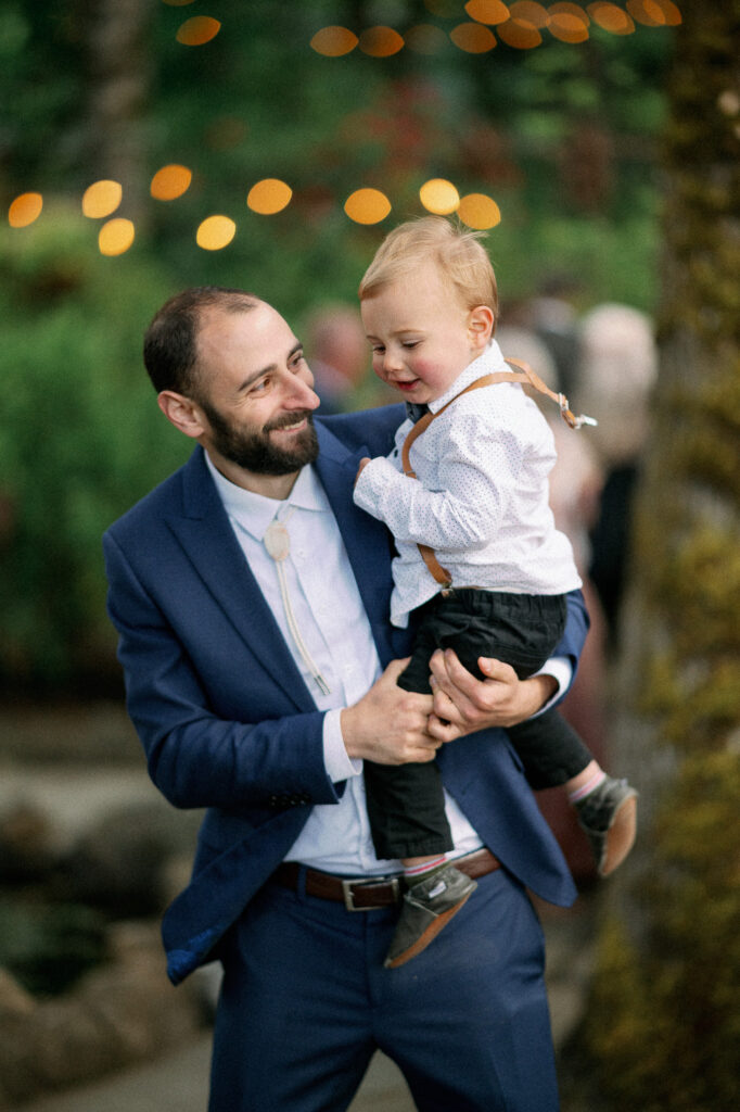 A guest holding a young child during the reception, smiling beneath string lights at the Griffin House.