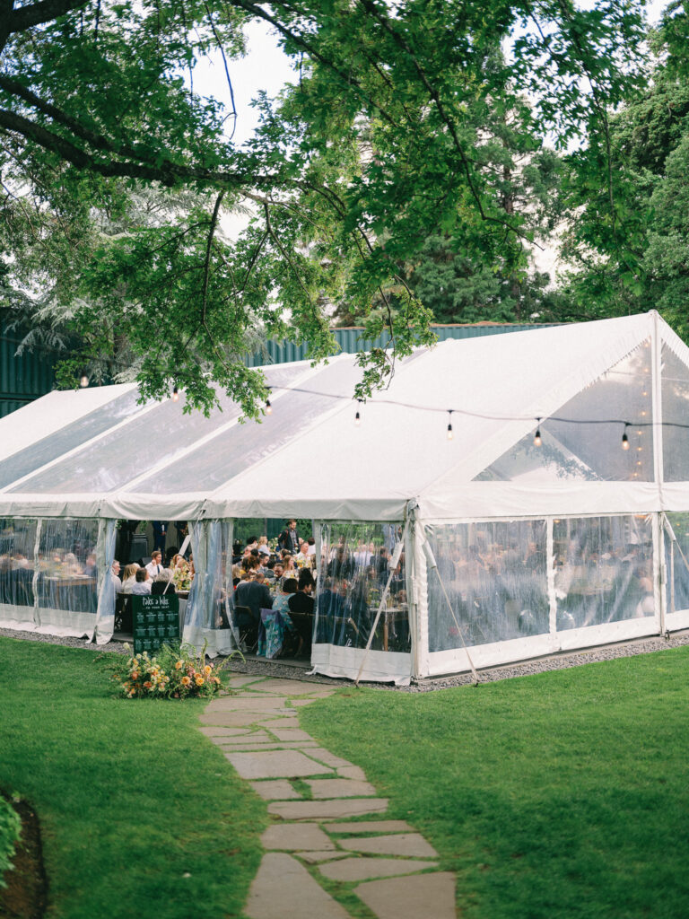 Clear reception tent at the Griffin House filled with guests during dinner, framed by trees and string lights.