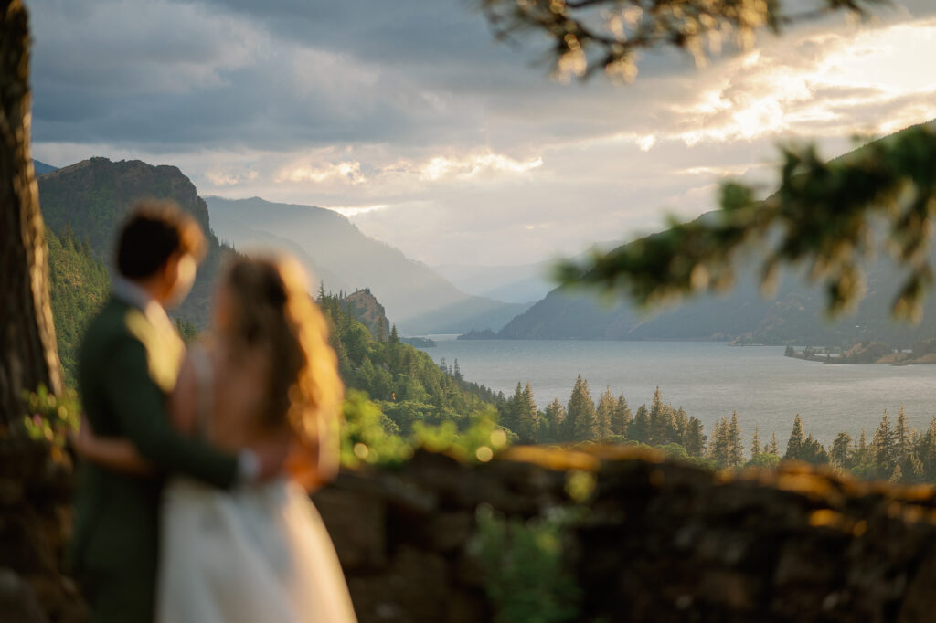 Golden hour view of the couple standing along a stone wall at the Griffin House, framed by trees and sweeping gorge views.