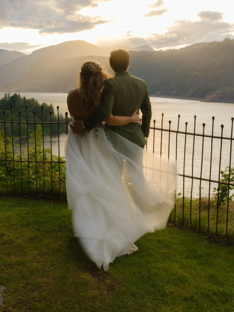 Wide scenic view of the Columbia River Gorge at sunset, with vineyards, forested hills, and the river reflecting warm evening light.