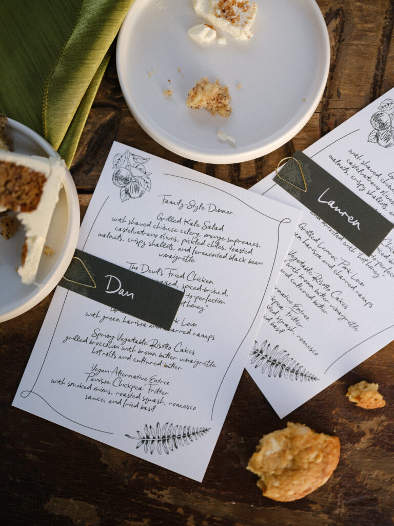 Close-up of handwritten dinner menus and place cards styled on a wooden table during a summer wedding at the Griffin House.