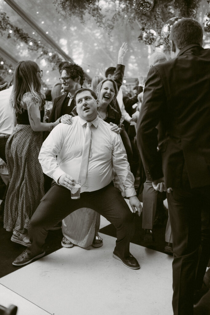 Black and white photo of guests dancing energetically on the checkered dance floor beneath a clear tent at the Griffin House.
