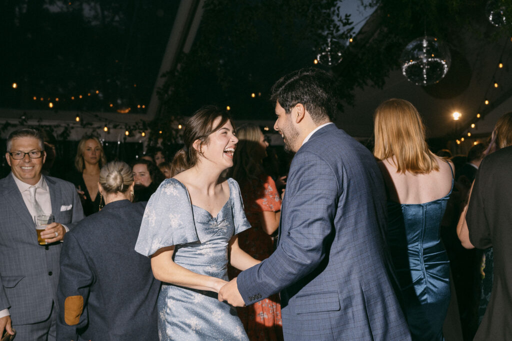 Guests dancing and laughing together during the wedding reception under string lights at the Griffin House.