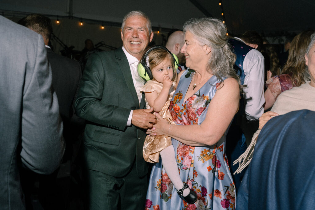 An older couple holding a young child wearing protective earmuffs on the dance floor during the Griffin House wedding reception.