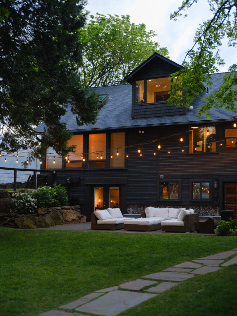 Exterior view of the Griffin House at dusk, with string lights glowing over outdoor lounge seating and the lawn.