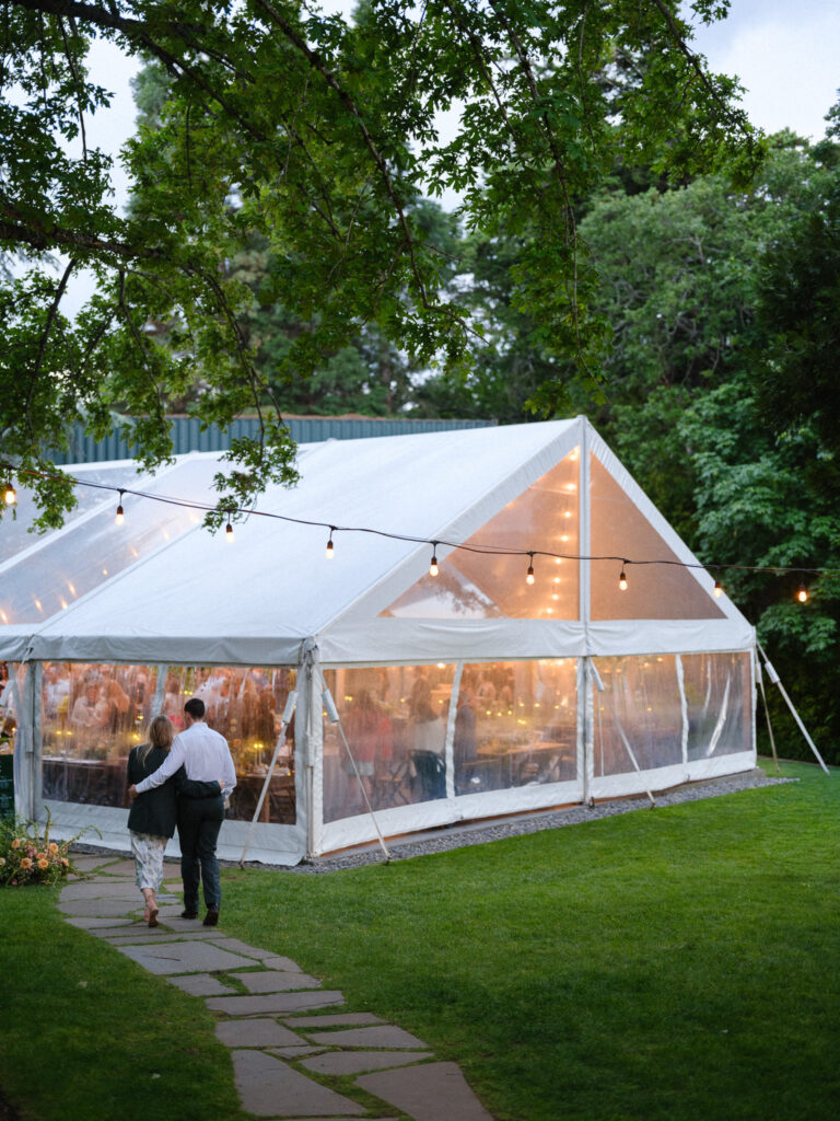 Exterior view of a clear reception tent glowing at dusk at the Griffin House, surrounded by trees and string lights.