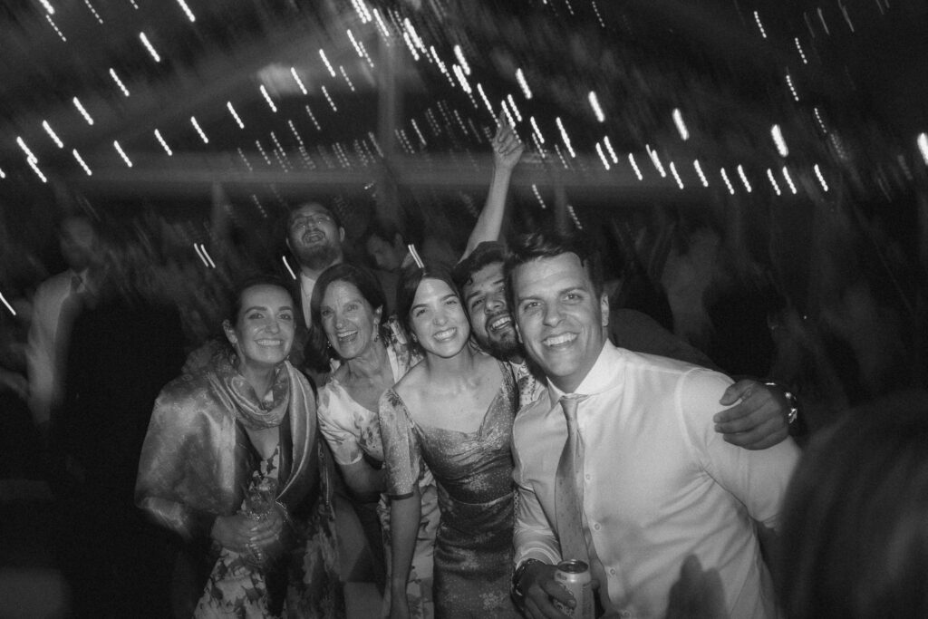 Black and white image of friends smiling and leaning together on the dance floor during the wedding reception.