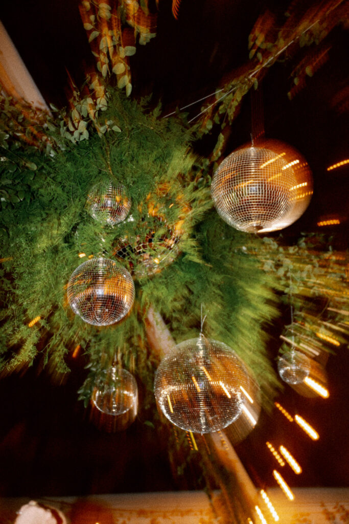 Close-up of hanging disco balls and greenery installation above the dance floor at the Griffin House wedding reception.