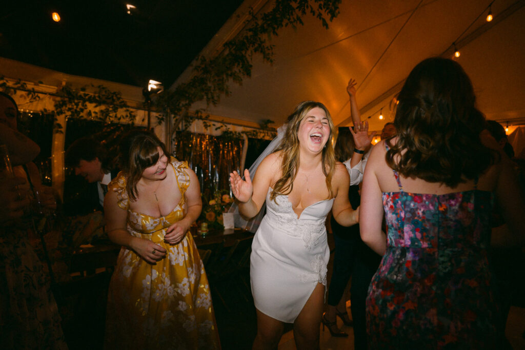 The bride laughing while dancing with friends during the reception beneath warm string lights at the Griffin House.