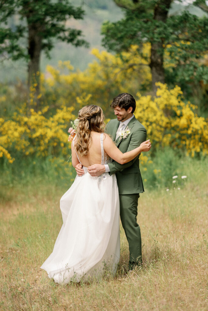 The couple holding each other during the first look at the Griffin House, surrounded by wildflowers and summer greenery.