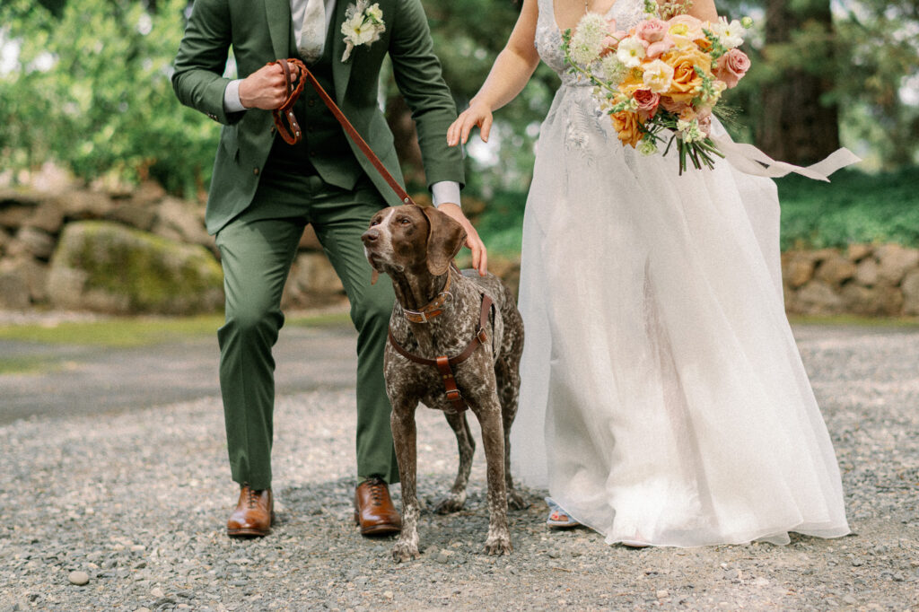 The couple standing with their dog on a leash, smiling together on a gravel path during their Griffin House wedding day.