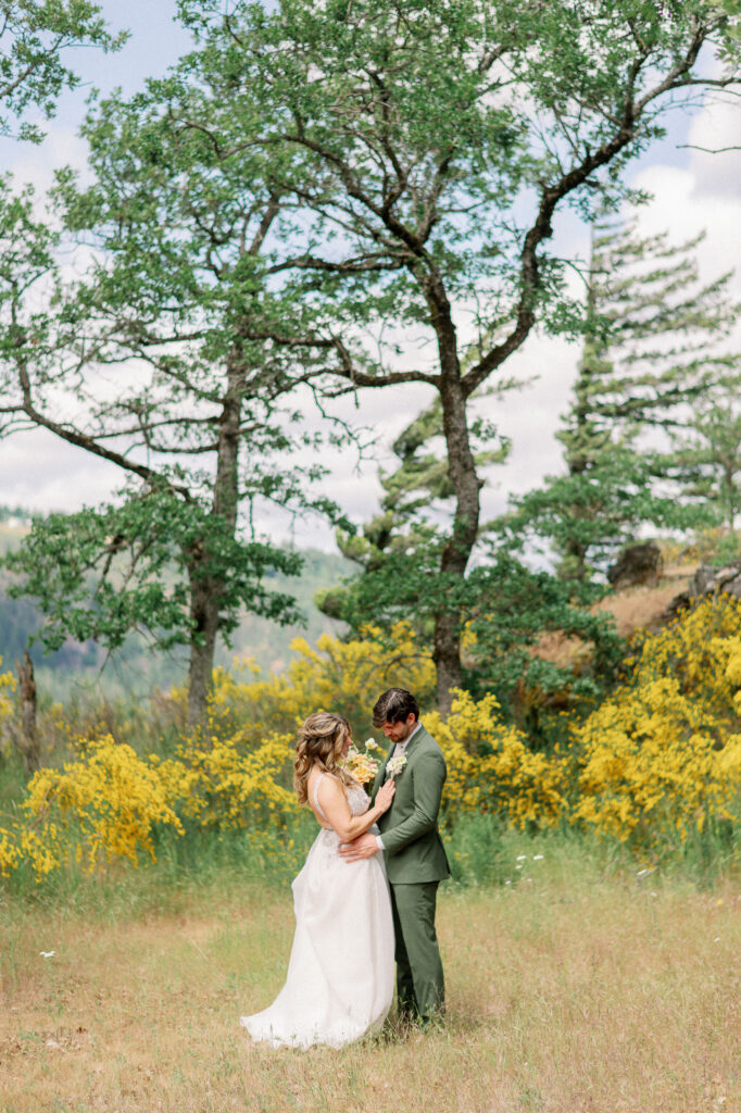 The couple embracing during their first look at the Griffin House, surrounded by yellow wildflowers and trees.