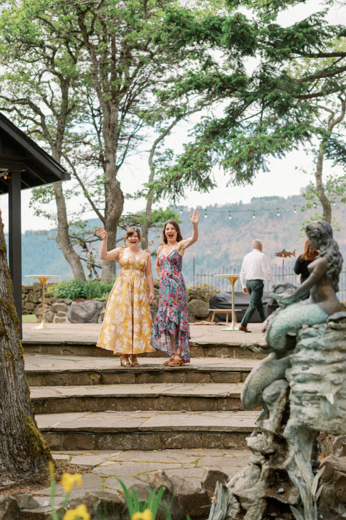 Wedding guests waving and laughing together on the stone terrace at the Griffin House during cocktail hour.