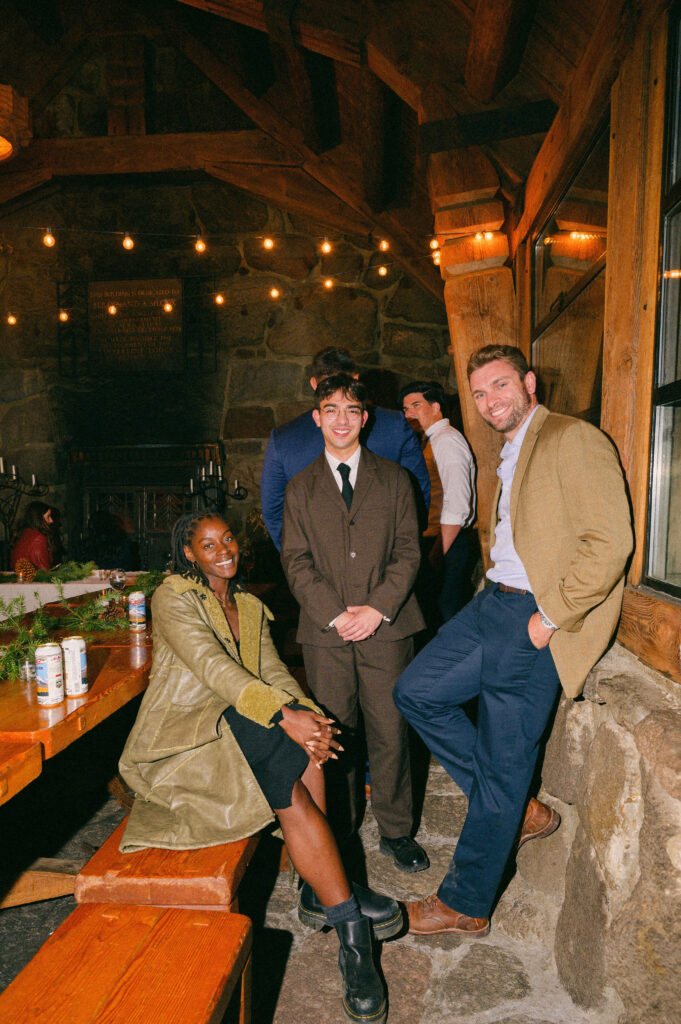 Wedding guests chat and laugh near the stone fireplace inside Silcox Hut, surrounded by warm lighting and rustic mountain charm.