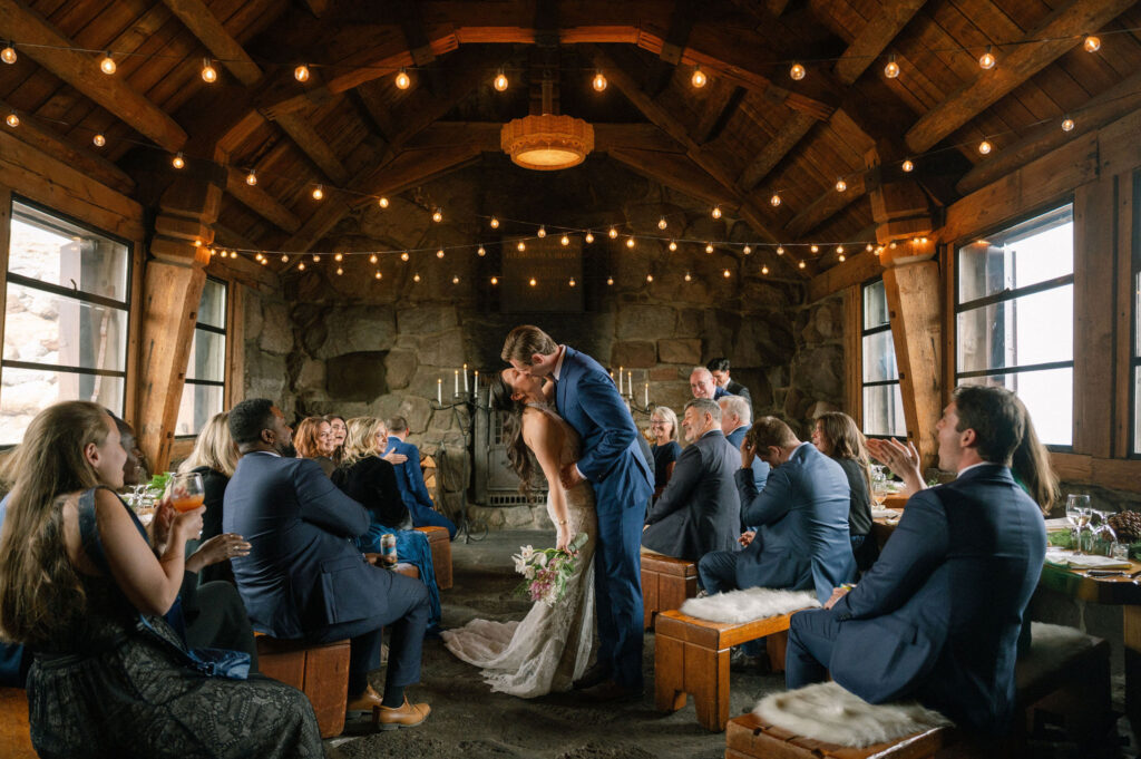 The bride and groom share their first kiss during their intimate Silcox Hut ceremony, surrounded by family and glowing candlelight.