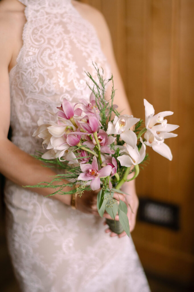 A detailed view of the bride’s orchid bouquet against her lace wedding gown inside Silcox Hut.
