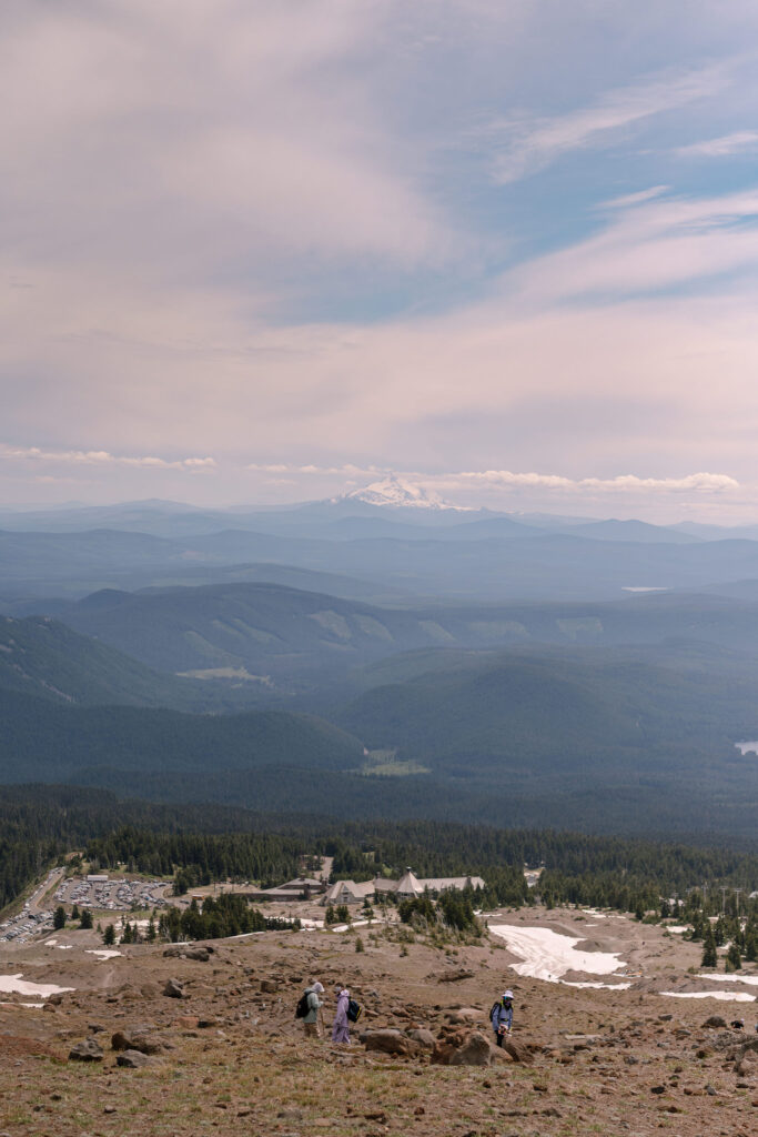 A sweeping view from high on Mount Hood, looking out over the Cascade Range and Timberline Lodge far below on a hazy summer day.