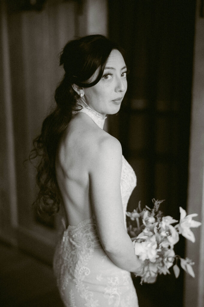 A black-and-white portrait of the bride glancing over her shoulder while holding her bouquet inside Silcox Hut.