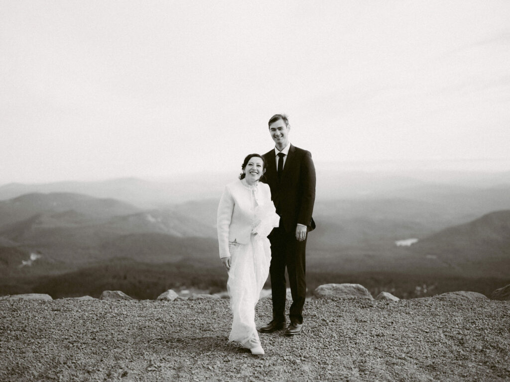 The bride and groom stand together on a ridge above Timberline Lodge, surrounded by expansive views of Oregon’s Cascade Range.