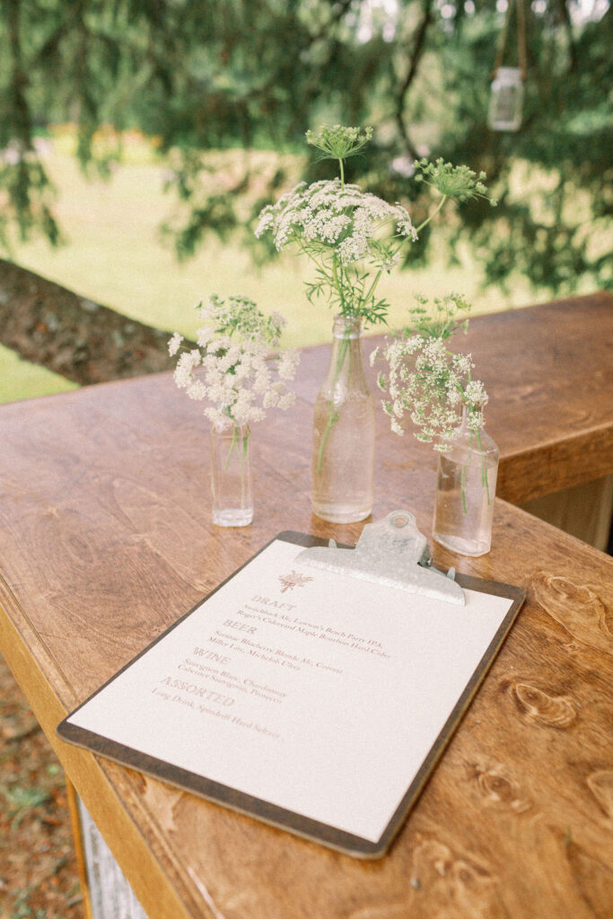 Small glass vases filled with Queen Anne’s lace flowers on a wooden bar beside a printed drink menu.