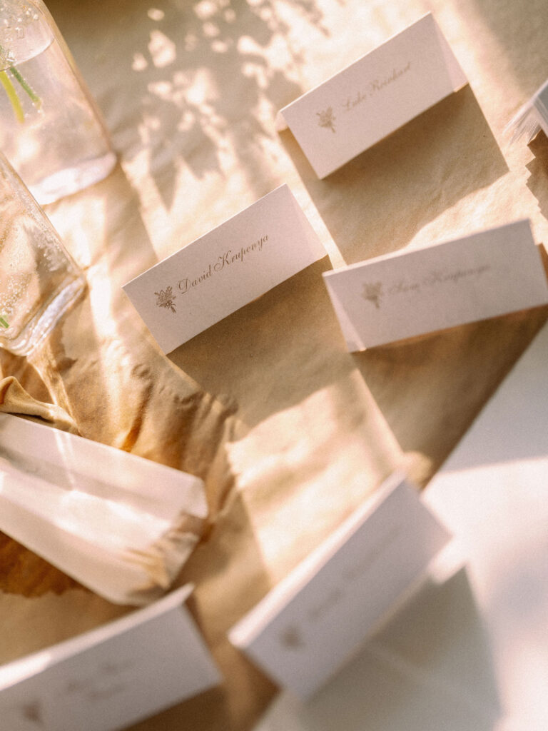 Close-up of handwritten wedding place cards arranged on a kraft-paper table runner in warm, dappled sunlight.