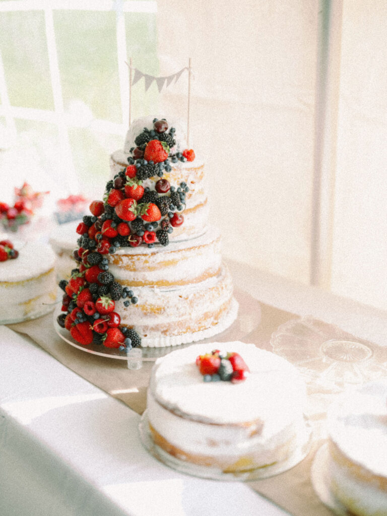 Tiered naked wedding cake adorned with cascading fresh berries, alongside smaller berry-topped cakes.