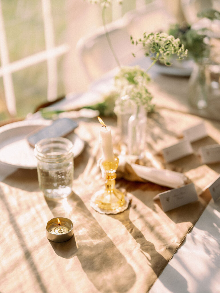 Softly lit reception table with burning candle, mason jar water glasses, and Queen Anne’s lace centerpieces.