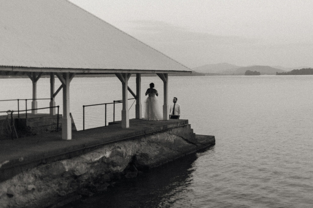 Bride and groom standing on the boathouse pier overlooking Lake Pleasant, framed by soft evening light and mountain silhouettes.