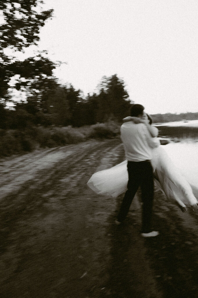 Motion-blurred photo of the groom spinning the bride on the lakeshore at sunset, her dress flowing dramatically.