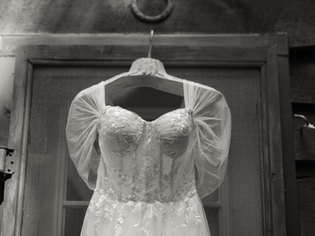Black-and-white close-up of the bride’s gown hanging on the cabin door, highlighting the embroidered bodice and sheer sleeves.