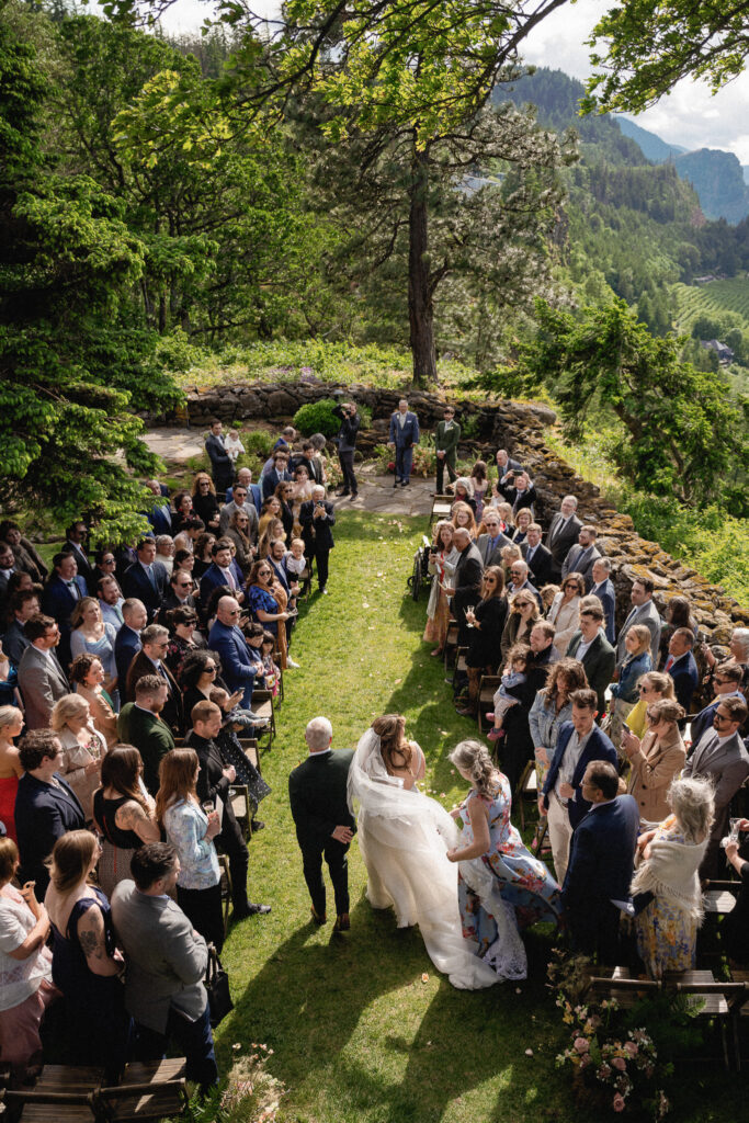 The couple walking back up the aisle after their ceremony at the Griffin House, surrounded by applauding guests.