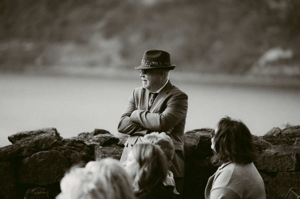 Black and white portrait of a guest watching the ceremony at the Griffin House, with the Columbia River visible beyond the stone wall.
