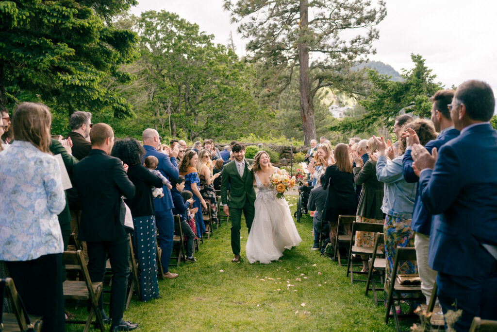 The newlyweds walking back down the aisle together at their outdoor Griffin House wedding, surrounded by applauding guests.