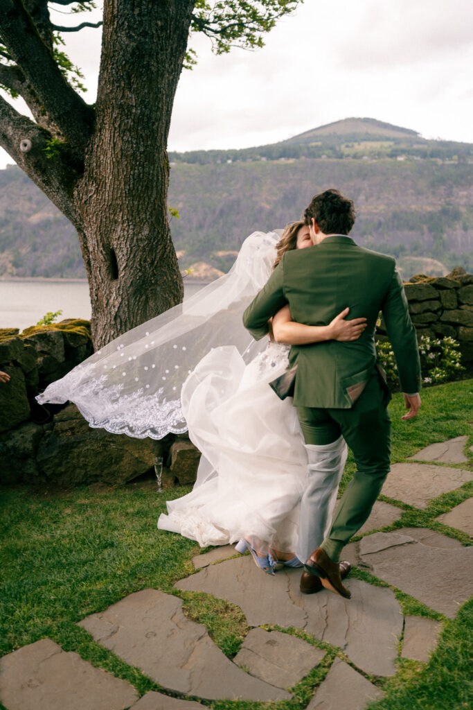The couple sharing a quiet embrace near the stone wall at the Griffin House, with Columbia River Gorge views behind them.