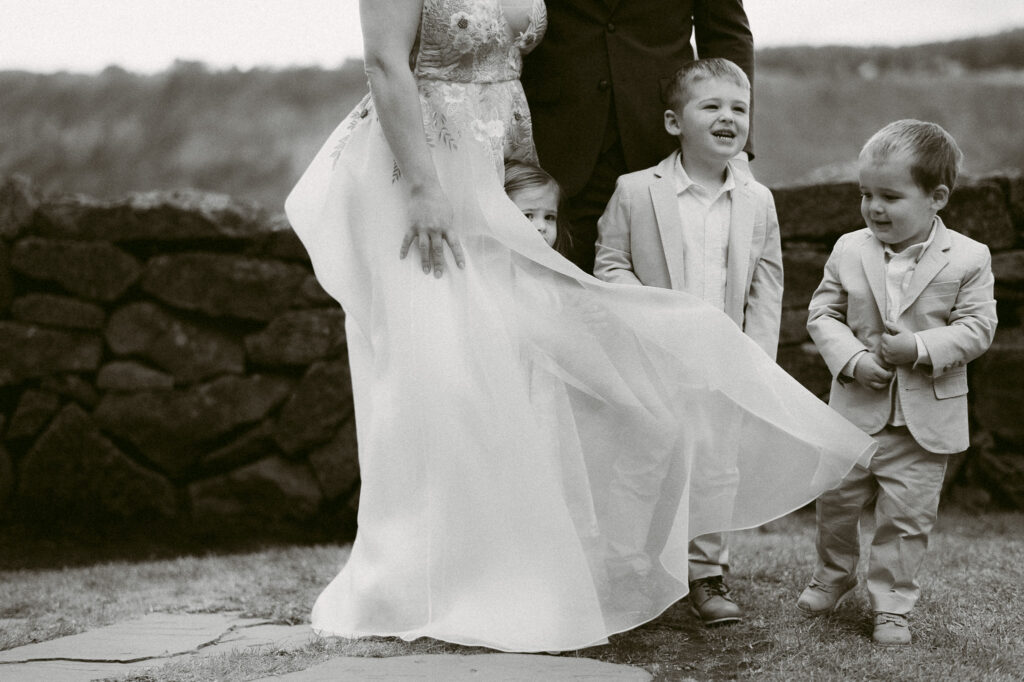 Black and white photo of children gathered around the bride’s dress during the wedding at the Griffin House.