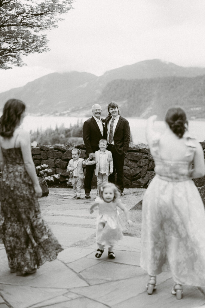 Black and white photo of wedding guests and children gathered near the stone wall at the Griffin House, with Gorge views beyond.