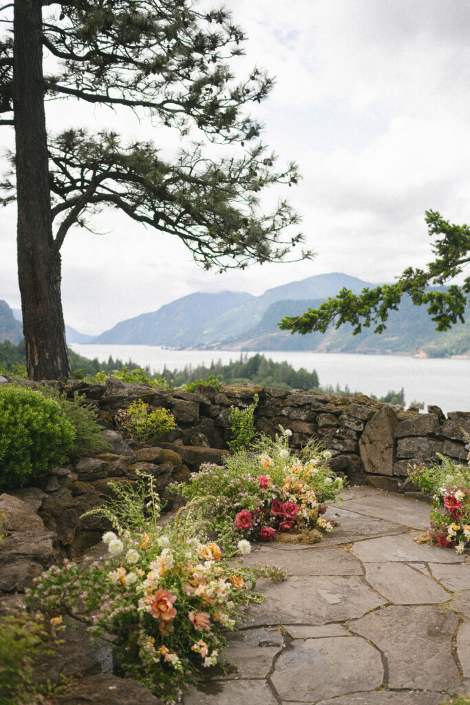 Stone terrace at the Griffin House overlooking the Columbia River Gorge, decorated with low floral arrangements for a summer ceremony.