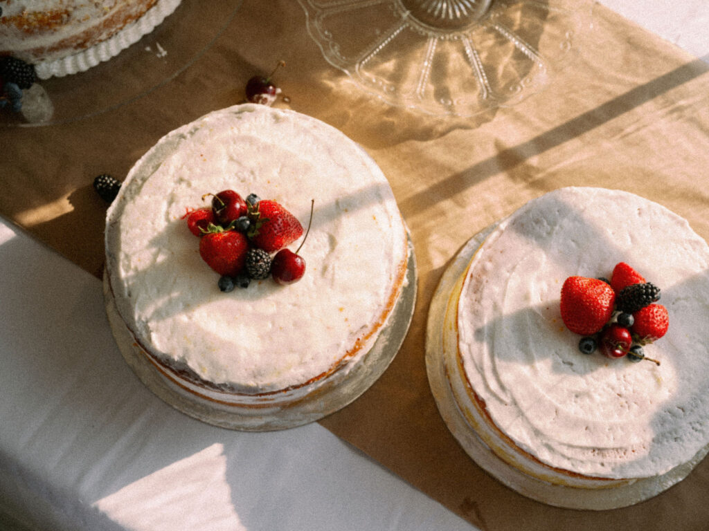 Two simple white wedding cakes topped with fresh summer berries, lit by warm late-day sun.