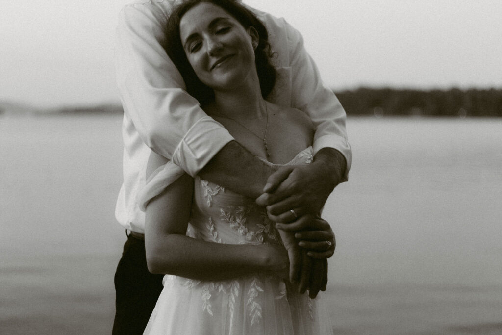 Close, intimate portrait of the bride smiling softly while wrapped in the groom’s arms beside Lake Pleasant.