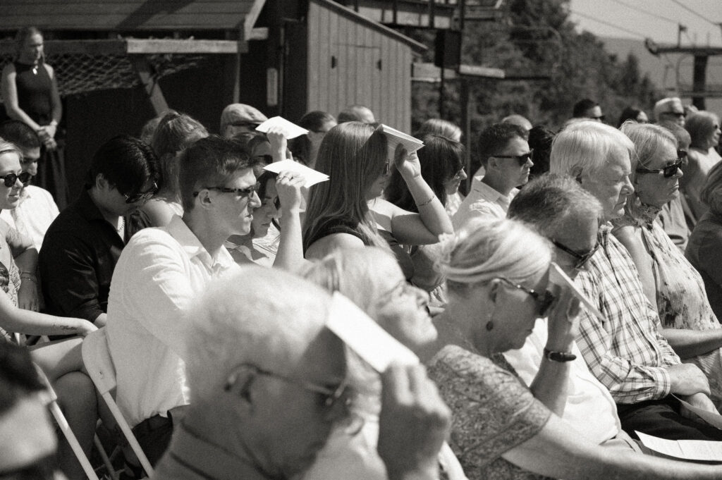 Black-and-white image of guests fanning themselves with programs and shading their eyes during the warm outdoor ceremony at Oak Mountain.
