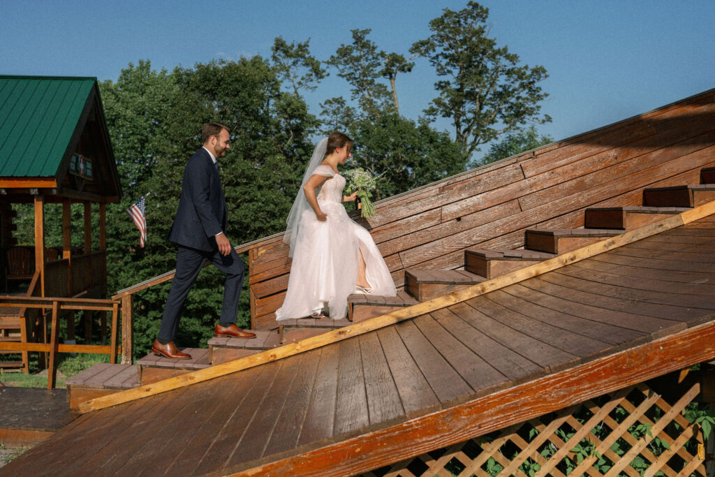 Bride and groom walking up the wooden steps of the Oak Mountain ski lift platform, holding her bouquet.