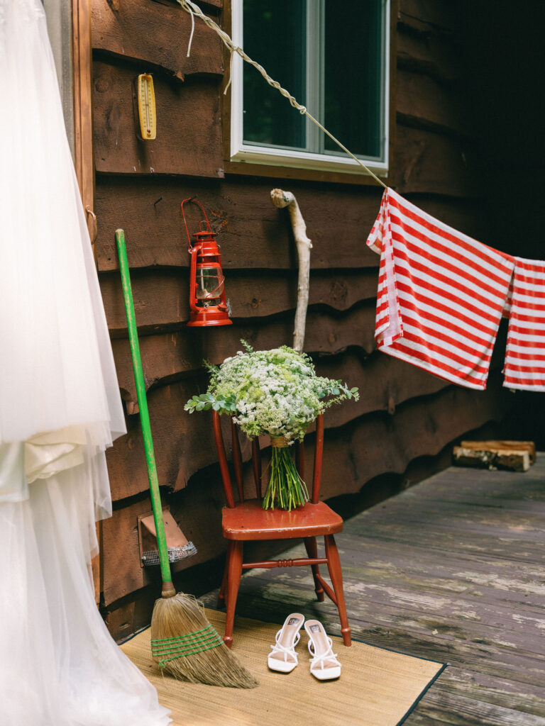 Bridal bouquet and white heels arranged on a red chair outside the family’s A-frame cabin in Speculator, NY, surrounded by rustic Adirondack details.