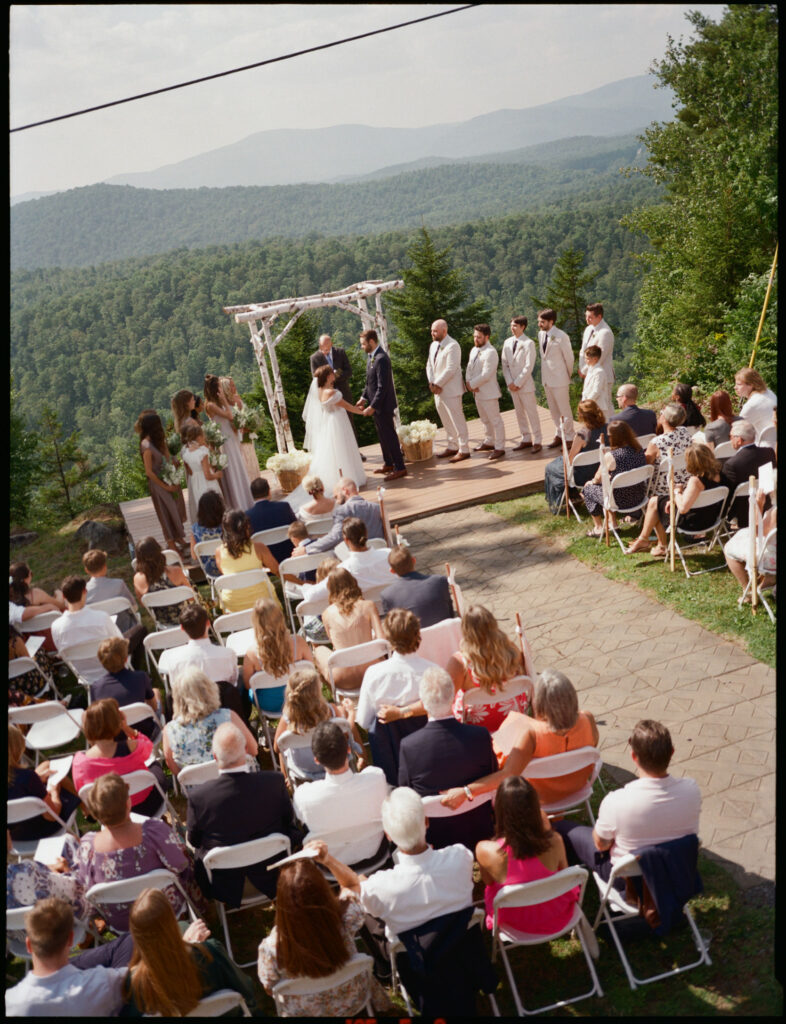 Film photograph of the wedding ceremony at Oak Mountain, with guests seated on the hillside and sweeping Adirondack mountain views behind the couple.