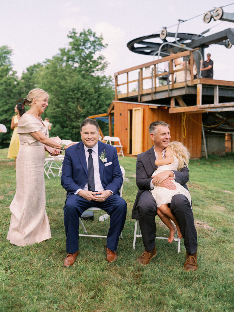 The bride’s parents and a guest sit together near the Oak Mountain lift station, smiling as the celebration continues around them.