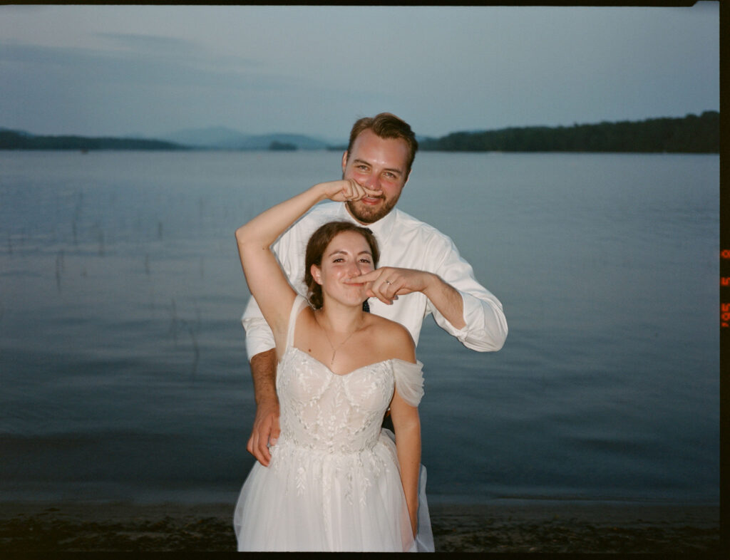 Film photo of the bride and groom posing playfully at the edge of Lake Pleasant during golden hour.