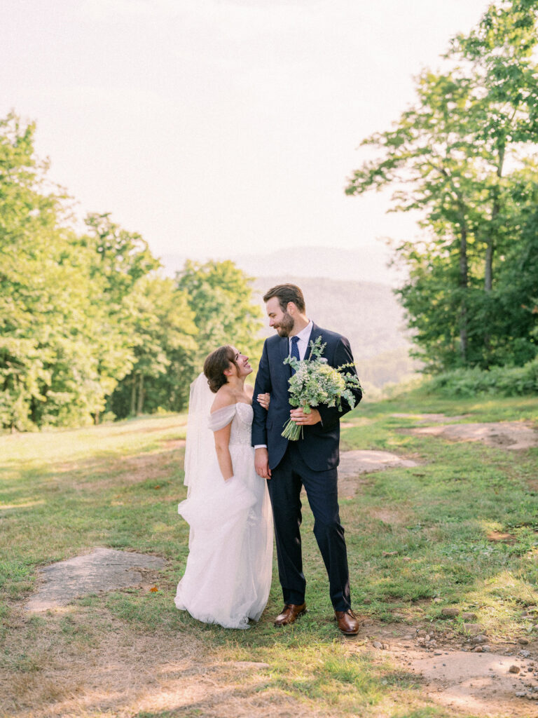 Bride and groom smiling at each other in soft afternoon light on a grassy mountain trail.