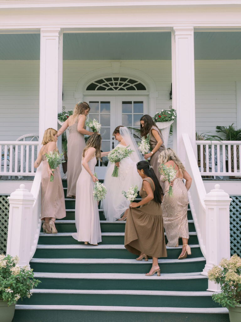 Bridesmaids gather around the bride on the steps of The White House on the Lake, helping arrange her gown and veil before the ceremony.